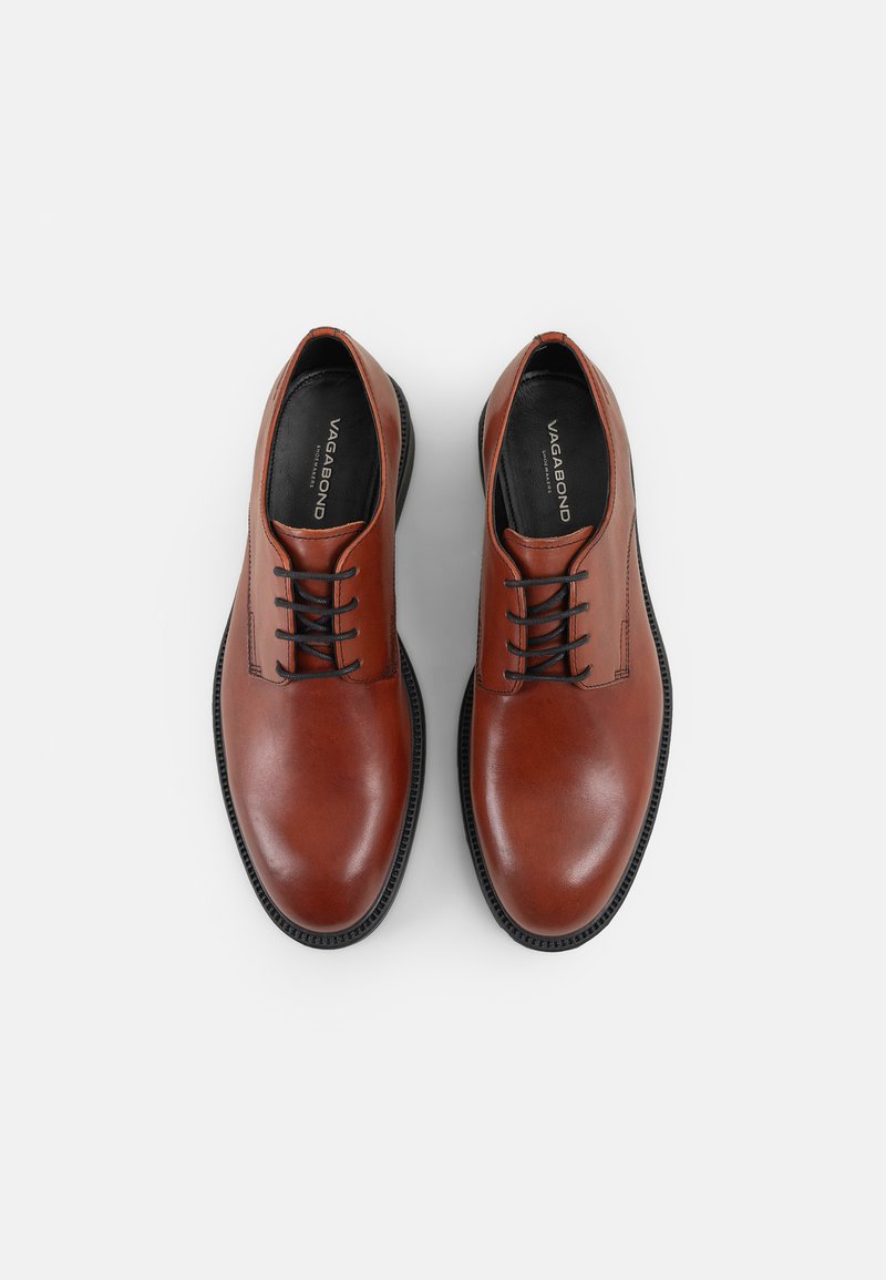 Brązowe skórzane buty o gładkim wykończeniu, okrągłym nosku i czarnych sznurowadłach. Charakteryzują się kontrastującą czarną podeszwą oraz subtelnymi liniami wzorniczymi.