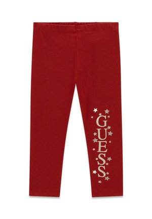 Leggings rouges avec des étoiles argentées et un texte vertical "GUESS" sur une jambe, avec une ceinture élastique et un design épuré.