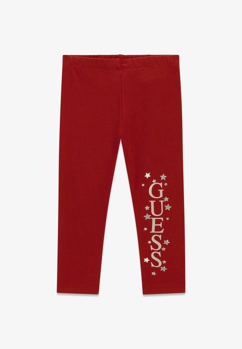Leggings rouges avec des étoiles argentées et un texte vertical "GUESS" sur une jambe, avec une ceinture élastique et un design épuré.