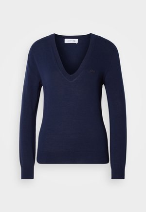 Marineblå V-hals genser med lange ermer, laget av glatt strikket stoff; har et lite brodert logo på brystet.