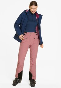 Giacca impermeabile blu navy con fodera rosa, maniche lunghe, pantaloni rosa con accenti neri, molteplici bottoni e tasche con zip.