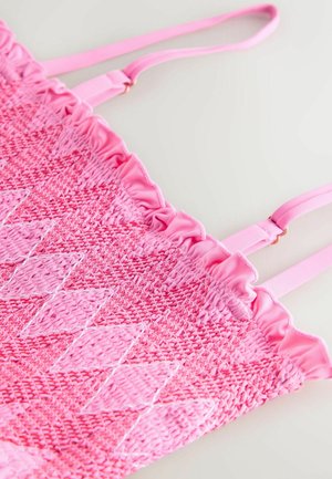 Vaaleanpunainen kudottu laukku, jossa on joustinneulosreunus yläosassa ja timanttikuvio. Säädettävät olkaimet ja sileä pinta parantavat muotoilua.