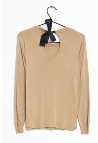 Long-sleeve, beige top with a round neckline and an open back, featuring a black bow tie detail at the neck. Soft fabric texture.