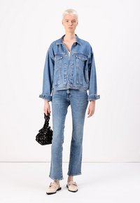 Giacca di denim con una vestibilità rilassata, di colore azzurro chiaro e grandi tasche; abbinata a jeans azzurri chiari aderenti e una borsa nera texturizzata.