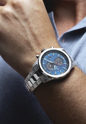 Montre en acier inoxydable argenté avec un cadran bleu, dotée de trois sous-cadrans, d'accents argentés et rouges, et d'un bracelet en métal.