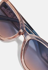 Occhiali da sole oversize con montatura trasparente rosa e lenti grigie sfumate. Presentano curve morbide e sottili strisce orizzontali sulle asticelle.