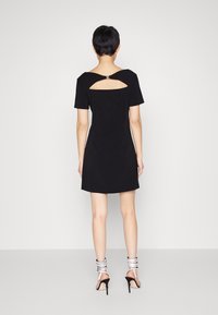 Vestido negro de manga corta con un corte cuadrado en la parte posterior. Tela suave con una silueta ajustada. Combinado con sandalias de tacón alto y tiras.