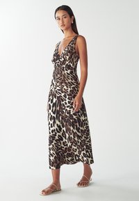 Wickelkleid mit Leopardenmuster, tiefem V-Ausschnitt, ärmellosem Design und fließender Silhouette. Glatter Stoff mit leichter Textur.