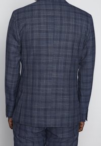 Marinblå rutig kostymjacka med en texturerad tygkvalitet och subtila ljusa accenter, enkel vent, och knäppta manschetter på ärmarna.