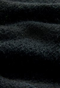 Schwarzer Stoff mit strukturierter Oberfläche, der geschichtete Wellen und feine Fasern aufweist und ein weiches, fusseliges Aussehen vermittelt.