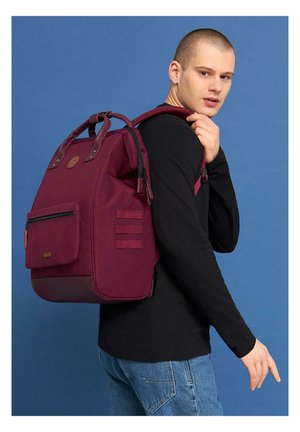 Sac à dos bourgogne en tissu durable, avec une poche zippée à l'avant, des poignées supérieures, des bretelles ajustables et des accents en sangle sur les côtés.