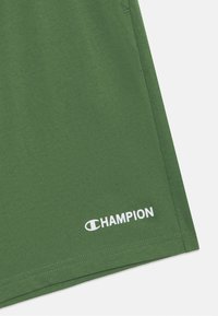 Groene katoenen shorts met een gladde textuur, voorzien van een wit "CHAMPION"-logo nabij de zoom en een schone, eenvoudige stikseldetails.