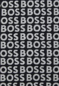 Sort stof med et gentaget mønster af ordet "BOSS" i fed hvide bogstaver, med en struktureret vævet overflade.
