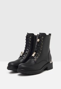 Bottes noires en cuir à la cheville avec un laçage à l'avant et des accents en métal doré. Talon épais et semelle texturée. Zip sur le côté pour un enfilage facile.