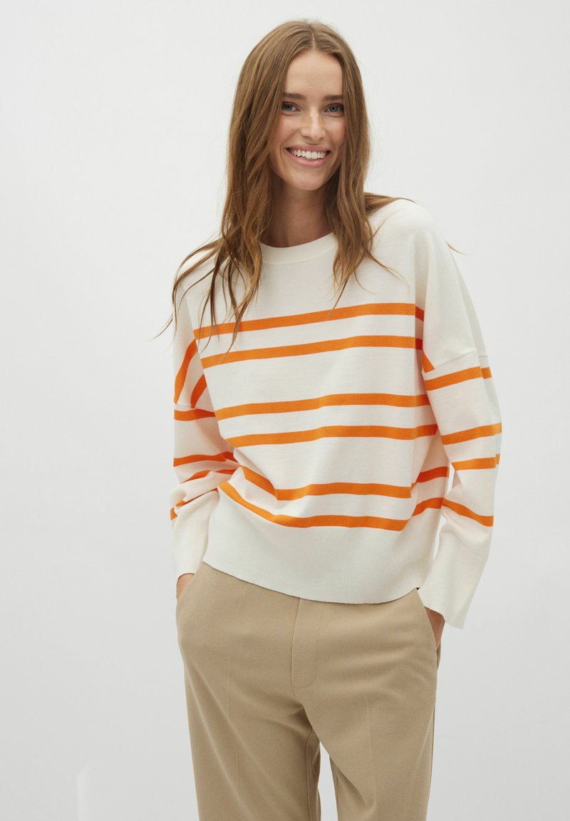 Gestreepte trui in crème met oranje en witte horizontale strepen. Voorzien van een relaxte pasvorm, ronde hals en lange mouwen. Gecombineerd met beige broeken.