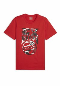 Červené bavlněné tričko s černobílým grafickým designem, který zahrnuje překrývající se text a cirkulární vzory na přední straně. Krátké rukávy, kulatý výstřih.