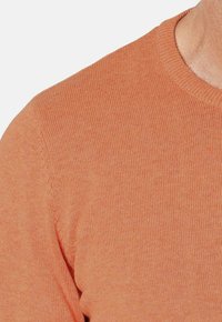 Suéter de punto naranja claro con cuello redondo y textura de canalé, mostrando un primer plano de la tela y el detalle de las mangas.