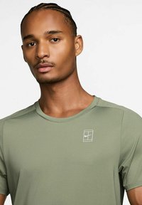 Olívazöld Nike sportpóló, rövid ujjú, kerek nyakkivágással, texturált anyagból készült, a bal felső oldalon fehér logóval.