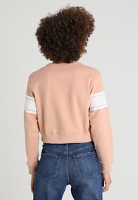 Felpa rosa tagliata con strisce bianche sulle maniche, realizzata in tessuto morbido, con collo rotondo e polsini a coste, abbinata a jeans blu.