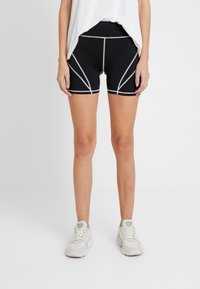 Czarne szorty sportowe z kontrastującymi jasnoszarymi szwami, z elastyczną talią i dopasowanym krojem. Noszone z luźną białą bluzką.