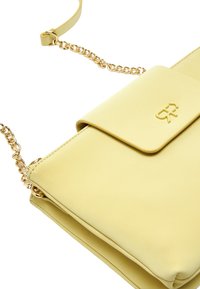 Żółta torebka z faux skórki z złotym łańcuszkiem, z klapą i wytłoczonym logo. Gładka faktura i prostokątny kształt z czystymi liniami.
