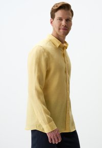 Camicia di lino gialla con colletto a bottone e maniche lunghe. Presenta una vestibilità comoda e una sottile texture. Design semplice, senza motivi.