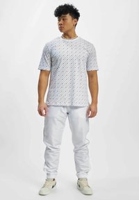 Weißes T-Shirt mit kurzen Ärmeln und einem Rautenmuster, kombiniert mit glänzenden weißen Jogginghosen mit schwarzen Seitenelementen und umgeschlagenen Säumen.