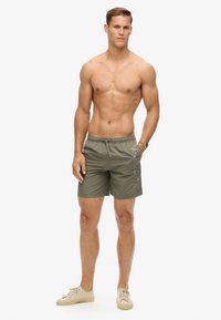 Costumi da bagno da uomo verde oliva, tessuto leggero, cintura elastica con cordino, tasche laterali, presenta stampa del logo sulla gamba sinistra.