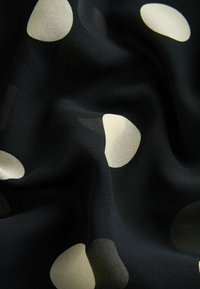 Tissu noir avec de gros pois blancs irréguliers, montrant des plis doux et une surface texturée.