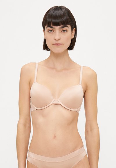 Beige gepolsterde bh met een gladde, matte textuur, verstelbare bandjes en een subtiele U-vormige halslijn. Gecombineerd met bijpassende low-rise slips.