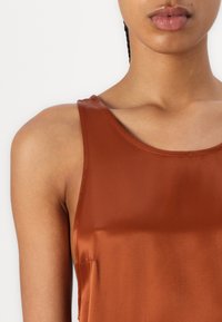 Brun sateng tanktop med en rund halslinning, med en glatt tekstur og tynne stropper. Designet inkluderer minimal skulderdekning.