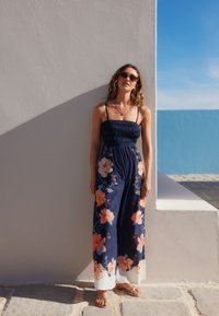 Rochie maxi bleumarin cu imprimeu floral în portocaliu și albastru, cu bodice strâns cu elastic, bretele reglabile și fustă fluidă cu tiv alb.