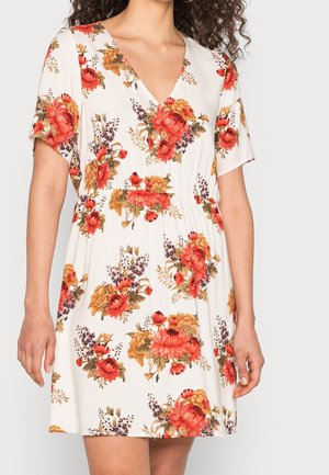 White short-sleeve dress with red, orange, and purple floral patterns, V-neckline, and fitted waist worn by a person with curly dark hair.