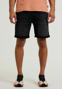 Zwarte denim shorts met opgerolde manchetten, aangevuld met een licht perzikkleurig T-shirt en multikleurige sportschoenen.