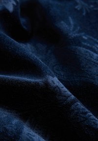 Tmavě modrá látka s měkkým, texturovaným povrchem. Vyznačuje se embosovaným vzorem, který vytváří jemný lesk na povrchu.