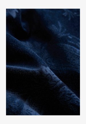 Dunkelblauem Stoff mit weichem, strukturiertem Finish. Enthält ein geprägtes Muster, das einen sanften Glanz über die Oberfläche erzeugt.