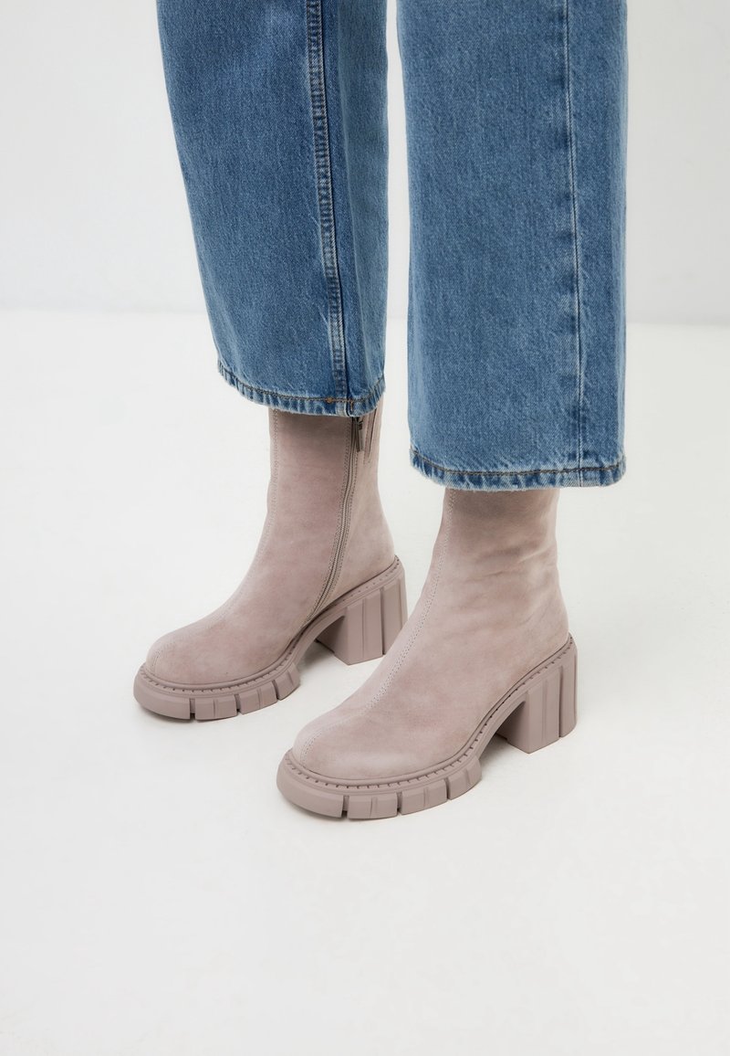 Bottes beiges en daim à la cheville avec un talon épais et texturé et une fermeture éclair latérale ; associées à un jean raccourci en denim clair.