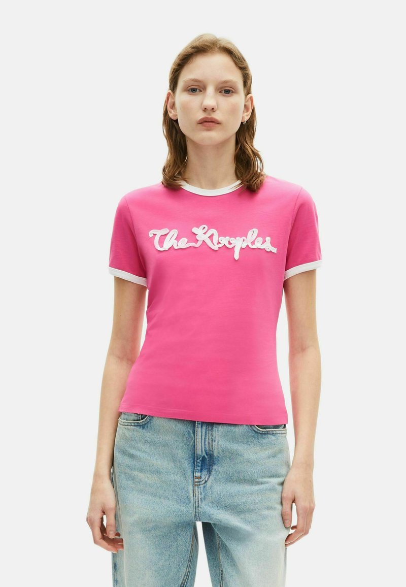 Roze katoenen t-shirt met korte mouwen, witte ribbels aan de rand en een opvallend wit scriptlogo met de tekst "The Kooples" op de voorkant.