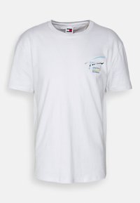 Camiseta de algodón blanca con cuello redondo, que presenta un pequeño gráfico colorido en el lado izquierdo del pecho que muestra texto estilizado y líneas.