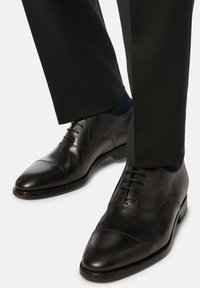 Scarpe eleganti in pelle nera con punta capitonné, dotate di una finitura liscia, chiusura con lacci e tacco leggermente rialzato.