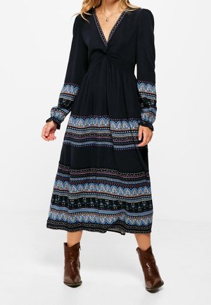 Robe longue noire avec décolleté en V, corsage torsadé et manches longues. Présente un ourlet à motifs en bleu et vert avec des accents décoratifs.