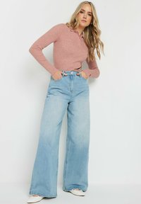 Ljusrosa ribbad långärmad polo skjorta i kombination med vida ljusblå denimjeans. Jeanserna har hög midja och sidfickor.