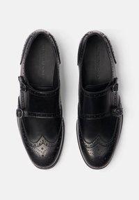 Scarpe in pelle nera con doppie fibbie, dettagli brogue, superficie liscia e punta arrotondata.