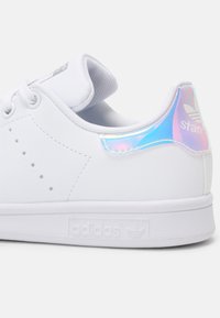 Beli usnjeni Adidas Stan Smith čevlji z iridescentnim poudarkom na peti, teksturirano podplat in perforirane detajle na straneh.