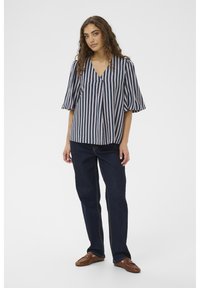 Bluza cu dungi în tonuri bleumarin și roz pal, cu decolteu în V și mâneci scurte bufante. Asortată cu blugi din denim închis și pantofi maro.