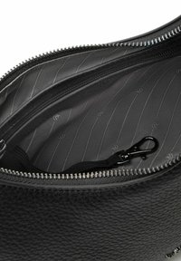 Interieur van een zwarte leren tas met een ritssluiting, een gladde voering met verticale strepen en een metalen clip om items vast te zetten.