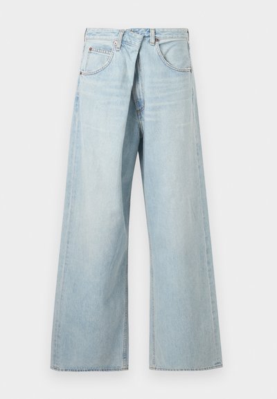 Világoskék, széles szárú farmernadrág övbújtatókkal és első zsebekkel, elölről egyszerű háttér előtt bemutatva.