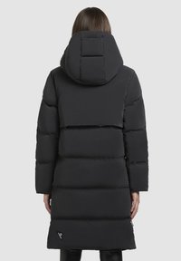 Melnā pūkainā mētelis ar lielu kapuci, kas raksturīgs ar quilted rakstu, garām piedurknēm un etiķetes akcentu tuvumā apakšmalai. Gluda, izolēta auduma.