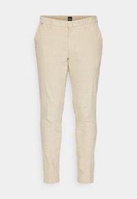 Béžové kalhoty na míru s texturovanou tkaninou. Mají klasické kapsy a úzký střih. Na pásu je viditelná značka.