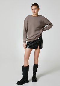 Brązowy sweatshirt, czarna minispódnica z ekoskóry z boku na zamek, oraz czarne kozaki za kolano na klamry. Gładka tekstura i dopasowany krój.